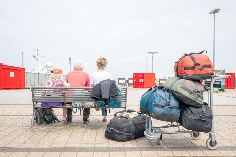 Eine dreiköpfige Familie wartet mit ihrem Gepäck am Fährhafen von Harlesiel auf die Abfahrt der Wangerooge-Fähre, um auf die Insel Wangerooge zu gelangen. Foto: DPA