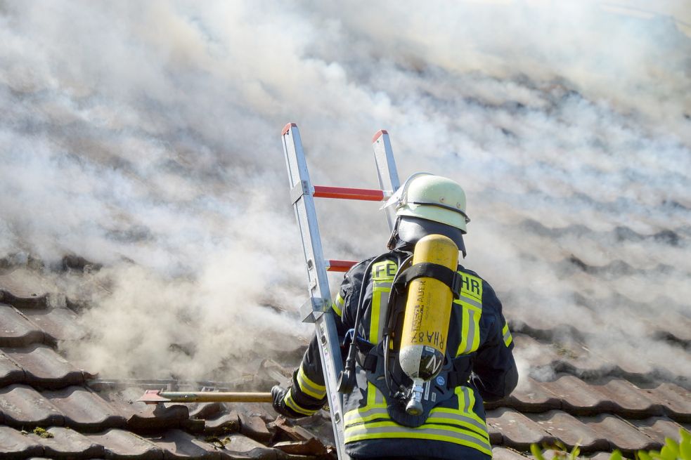 Ein Feuerwehrmann nimmt Dachziegel herunter, um an Glutnester heranzukommen. Foto: Weers