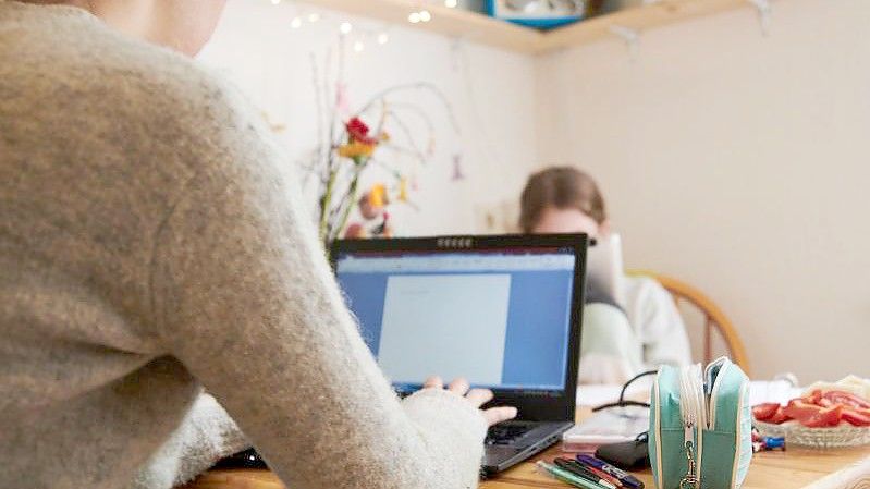 Eine Mutter arbeitet am Küchentisch während ihre Tochter gegenüber in ein Tablet guckt. Foto: Annette Riedl/dpa