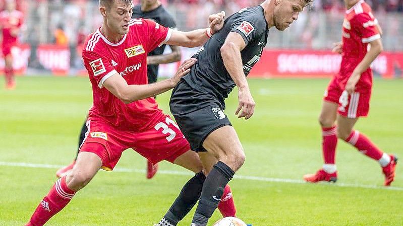 Augsburgs Florian Niederlechner (r) schirmt den Ball gegen den Unioner Robin Knoche ab. Foto: Andreas Gora/dpa