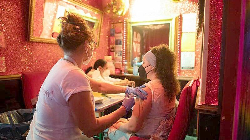 Eine junge Frau lässt sich in einer Bar nahe der Reeperbahn im Hamburger Stadtteil St. Pauli gegen das Coronavirus impfen. Foto: Daniel Reinhardt/dpa