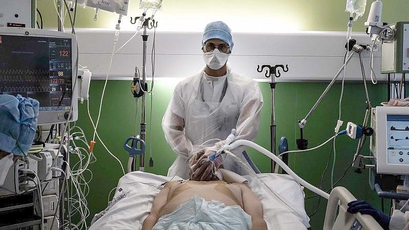 Ein medizinischer Angestellter (M) kümmert sich auf der Intensivstation eines Krankenhauses in Pierre-Benite um einen Corona-Patienten. Foto: Jeff Pachoud/AFP/dpa