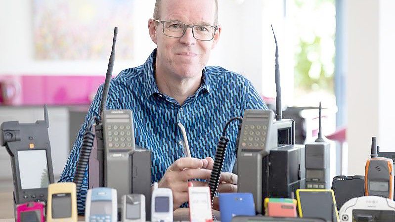 Auf dem vom Mobile Phone Museum herausgegebenen Foto sitzt Ben Wood, Gründer des Museums und Analyst des Unternehmens CCS Insight, hinter einigen der über 2.000 einzigartigen Mobiltelefone, die Teil des Online-Museums sein werden. Foto: Mobile Phone Museum/Vodafone/PA Media/dpa