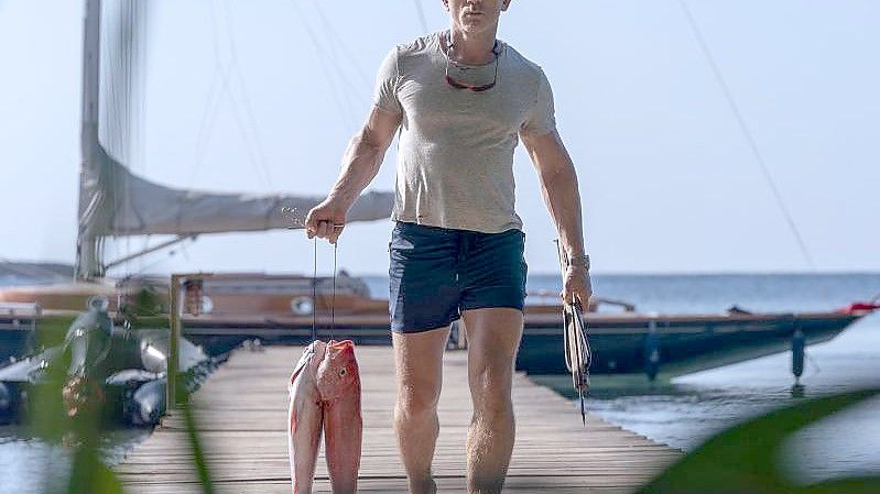 Daniel Craig als James Bond mit Fischen in der Hand in einer Szene des Films "James Bond 007 - Keine Zeit zu sterben". Foto: Nicola Dove/Universal Pictures/dpa