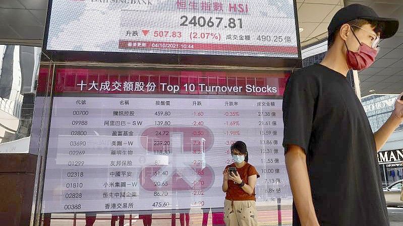 Menschen an der elektronischen Tafel einer Bank, die den Aktienindex an der Hongkonger Börse anzeigt. Foto: Vincent Yu/AP/dpa