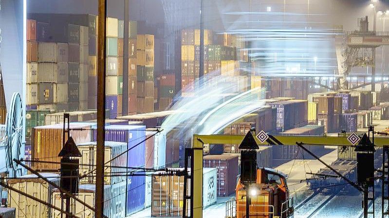 Am Containerbahnhof Frankfurt-Ost stehen am frühen Morgen hunderte Container, während im Vordergrund ein Kran einen weiteren von einem angekommenen Güterzug hinzufügt. Foto: Frank Rumpenhorst/dpa
