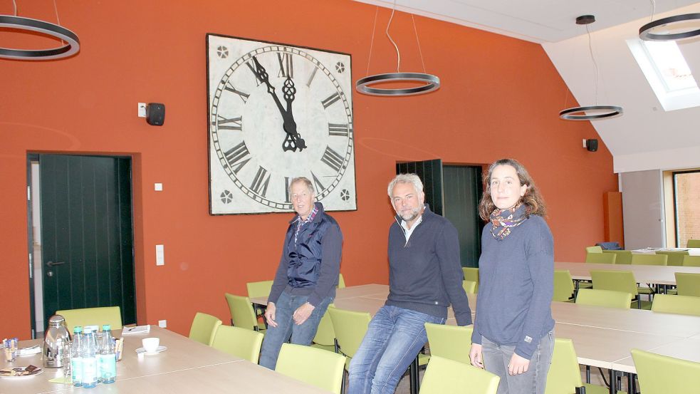 Im neu angebauten großen Saal hängt die alte Turmuhr an prominenter Stelle. Gerhard Evers (von links) vom Kirchenvorstand, Architekt Jann Kersten und Pastorin Katrin Krüger war es wichtig, im denkmalgeschützten Haus Modernes und Historisches zu kombinieren. Foto: Karin Böhmer