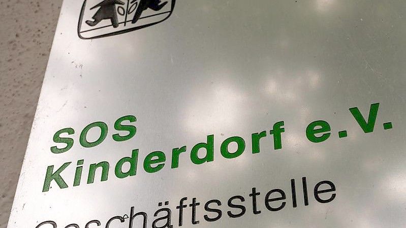 Das Logo und der Schriftzug "SOS Kinderdorf e.V. Geschäftsstelle" ist auf einem Schild zu sehen. Nach Bekanntwerden von Übergriffen in einem SOS-Kinderdorf haben sich weitere mutmaßliche Betroffene gemeldet. Foto: Peter Kneffel/dpa