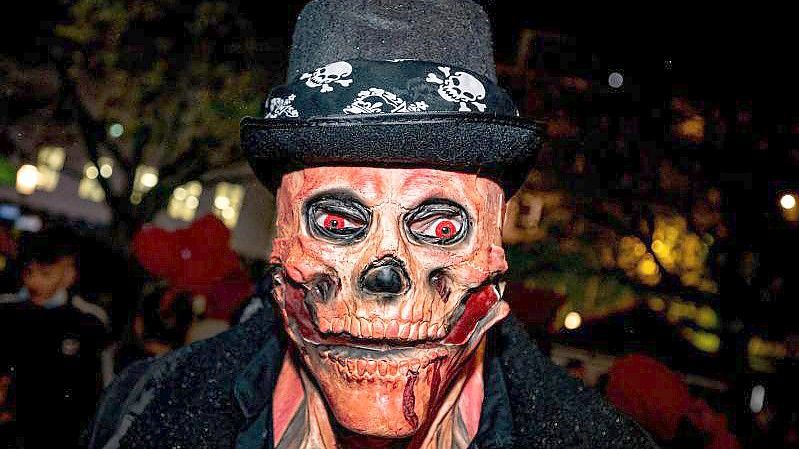 Ein Mann mit einer Totenkopf-Maske und glühenden roten Augen bei der Essener Halloween-Parade. Neben fantasievollen Kostümen gab es in der Nacht in Teilen Deutschlands auch Ruhestörungen, Böllerwürfe und Ausschreitungen. Foto: Malte Krudewig/dpa