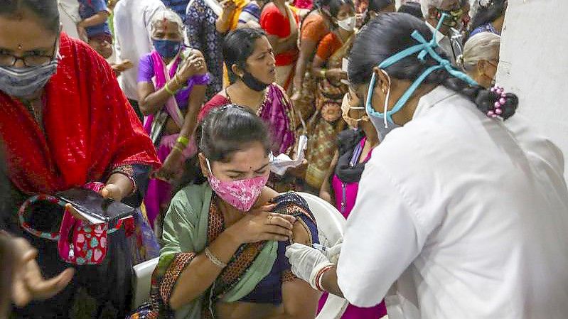 Eine Mitarbeiterin des Gesundheitswesens verabreicht eine Dosis mit dem Corona-Impfstoff Covaxin, während Hunderte von Menschen anstehen, um ihre zweite Dosis des Impfstoffs im städtischen Stadion in Hyderabad zu erhalten. Foto: Mahesh Kumar A/AP/dpa
