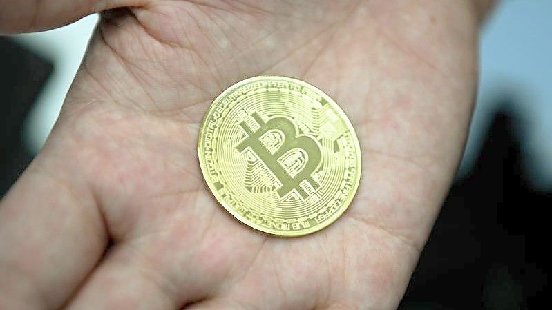 Ein Mann hält eine nachgemachte Münze mit dem Bitcoin-Logo in den Händen. Foto: Nicolas Armer/dpa