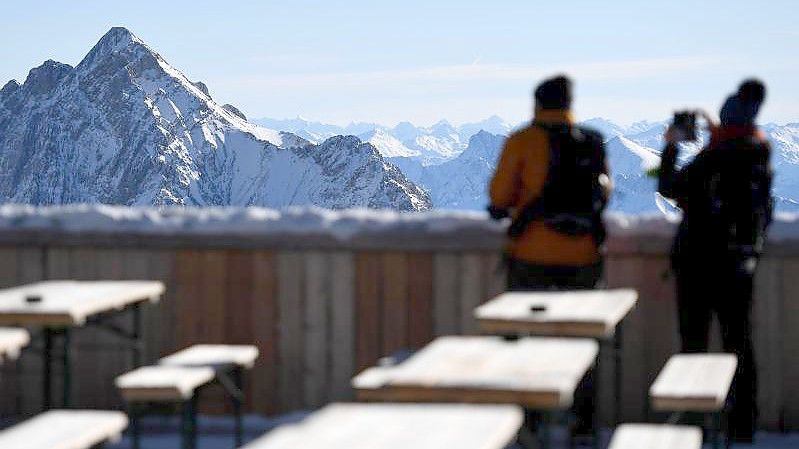 Zwei Besucher fotografieren von der Zugspitze aus das Panorama des Wettersteingebirges. Nach gut eineinhalbjähriger Pause wegen Corona sollen dort wieder Lifte laufen und Skifahrer ihre Schwünge ziehen. Foto: Angelika Warmuth/dpa