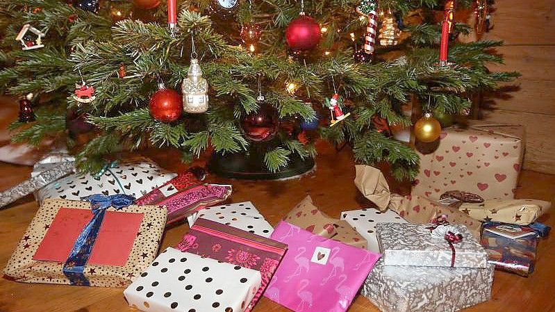 Verpackte Weihnachtsgeschenke liegen in einem Wohnzimmer unter einem geschmückten Weihnachtsbaum. Foto: Karl-Josef Hildenbrand/dpa
