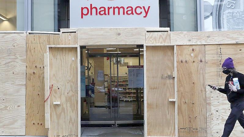 Ein Mann geht in Boston an einem mit Brettern vernagelten Geschäft der CVS-Apotheke vorbei. (Archivbild). Foto: Michael Dwyer/AP/dpa