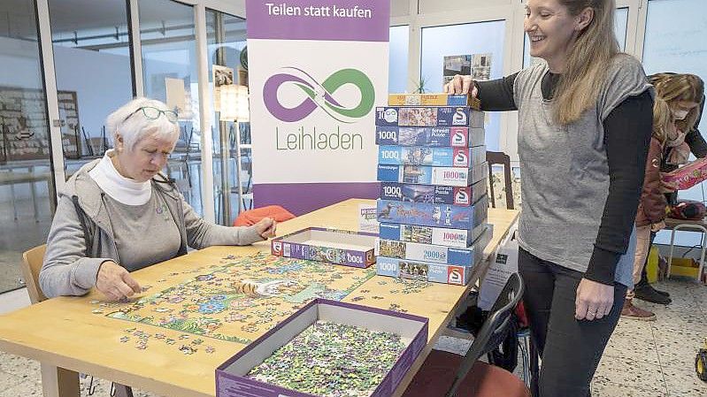 Die freiwilligen Mitarbeiterinnen Anne Deneke (l) und Dana Lorentz-Sengöz stehen vor einem Stapel Puzzles, die man ausleihen kann. Foto: Frank Rumpenhorst/dpa