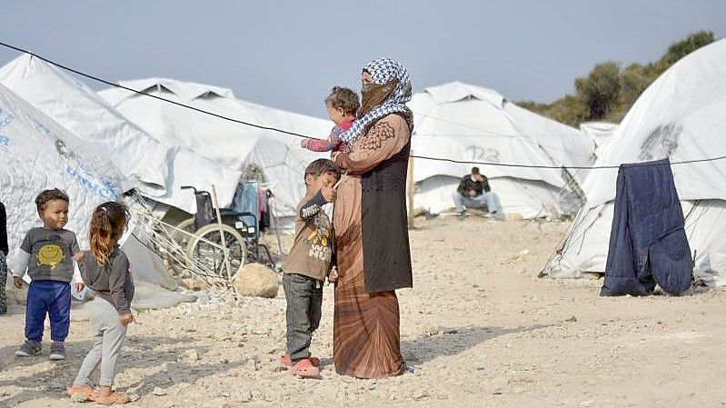 Eine Frau steht mit einem Baby im Arm und drei kleinen Kindern im Flüchtlingslager Kara Tepe in der Nähe von Mytilini auf Lesbos zwischen Zelten. Foto: Panagiotis Balaskas/AP/dpa