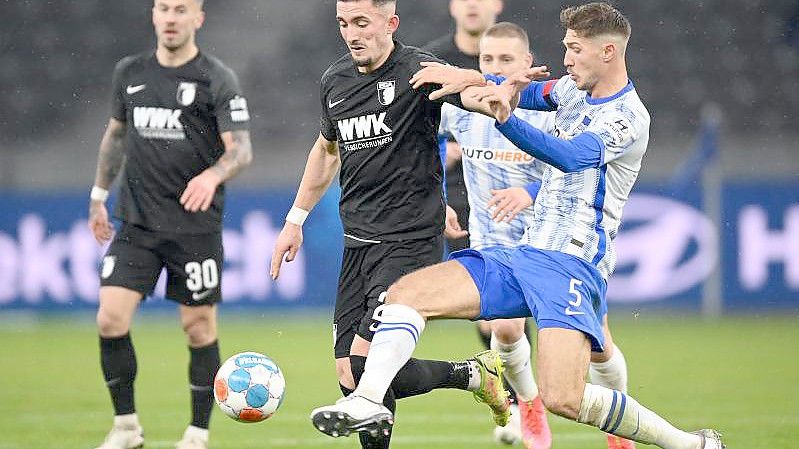 Herthas Niklas Stark (r) gegen Augsburgs Andi Zeqiri (M) kämpfen um den Ball. Foto: Soeren Stache/dpa-Zentralbild/dpa