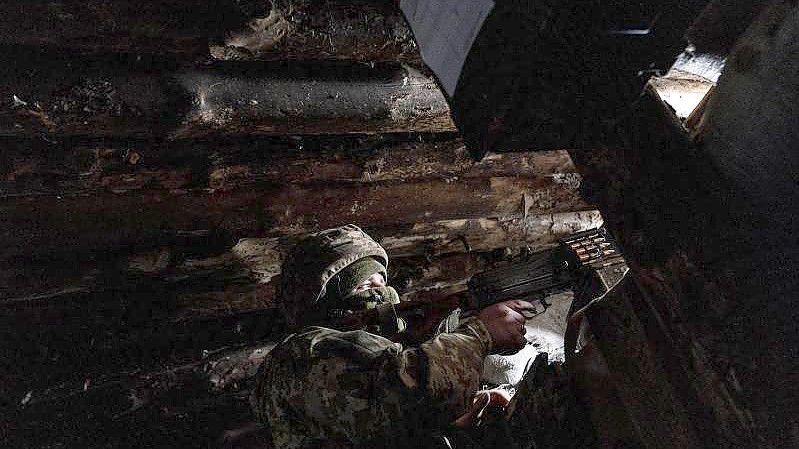 Ein ukrainischer Soldat hält sich schussbereit mit einem Maschinengewehr in einem Unterschlupf auf. Foto: Evgeniy Maloletka/AP/dpa/Archiv