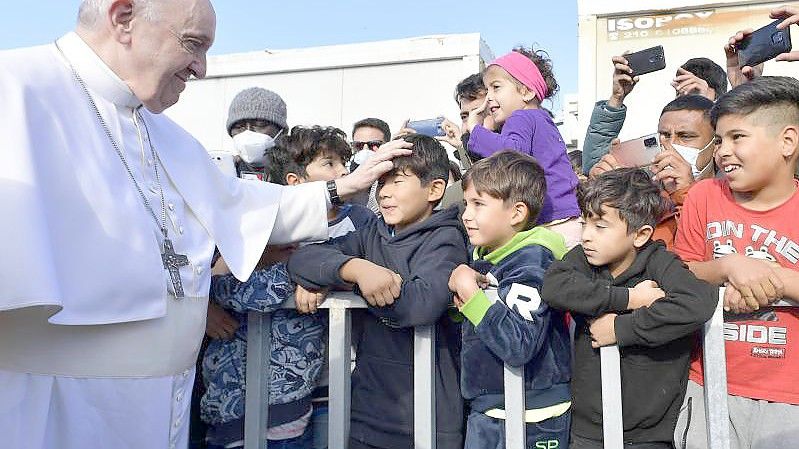 Papst Franziskus (l) legt einem Jungen im Flüchtlingslager auf der Insel Lesbos die Hand auf den Kopf. Foto: Vatican Media/ANSA via ZUMA Press/dpa