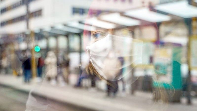 Eine Frau mit Mund-Nasen-Schutz spiegelt sich im Fenster einer Straßenbahn an der Konstablerwache in der Frankfurter Innenstadt. Foto: Frank Rumpenhorst/dpa