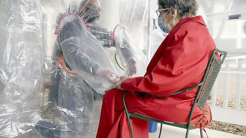 Gregg MacDonald hält in einem sogenannten „Umarmungszelt“ im US-Bundesstaat Kentucky die Hand seiner 84-jährigen Mutter Chloe. Seit Pandemiebeginn sind in den USA mehr als 800.000 Menschen am Coronavirus gestorben. Foto: Thomas Peipert/AP/dpa