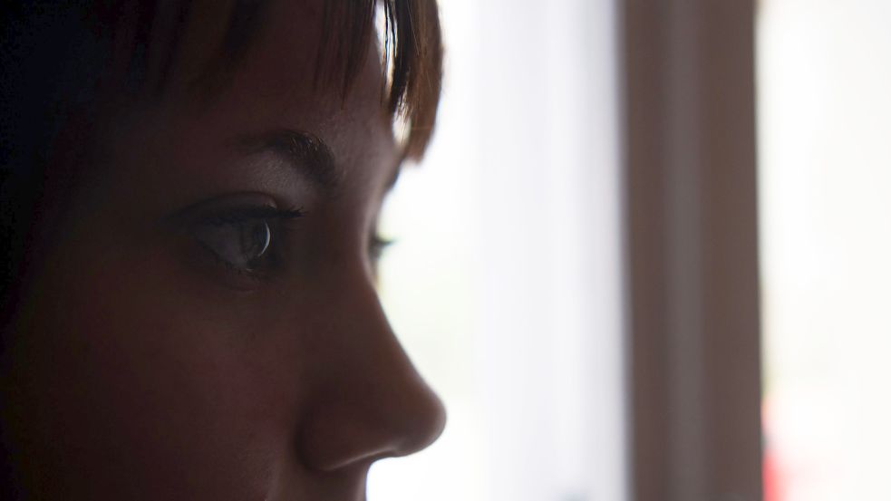Eine Jugendliche steht in einem abgedunkeltem Raum am Fenster. Foto: DPA