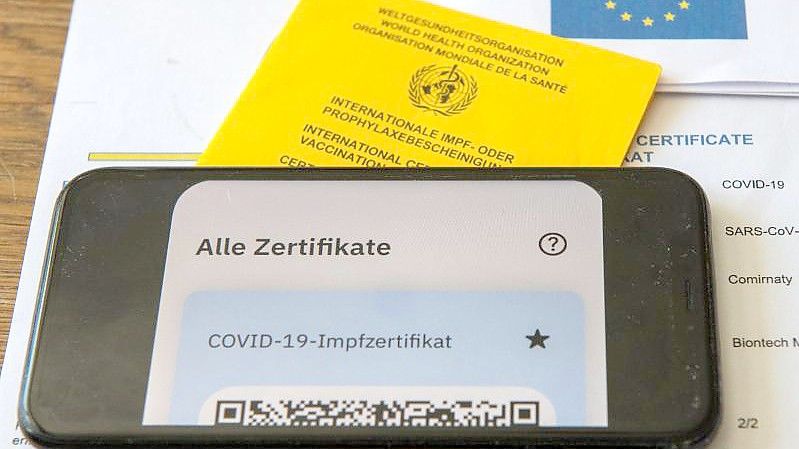 Ein Impfpass und ein Smartphone, auf dem die App CovPass läuft, liegen auf einem Impfzertifikat, das von einer Apotheke ausgestellt wurde. Foto: Stefan Puchner/dpa