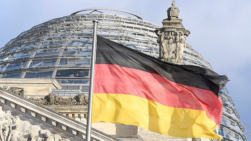 Die schwarz-rot-goldene Flagge vor der Kuppel des Reichstages. Foto: picture alliance / Soeren Stache/dpa