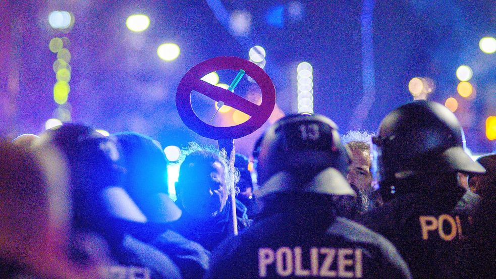 Polizisten und und Demonstranten stehen sich in der Innenstadt von Magdeburg gegenüber. Dabei trägt ein Demonstrant eine Schild, das eine durchgestrichene Spritze zeigt. Bundesweit gingen zu Wochenbeginn Zehntausende auf die Straßen, um gegen Corona-Maßnahmen zu protestieren. Nicht immer blieben die Aufzüge friedlich. Foto: Klaus-Dietmar Gabbert/dpa