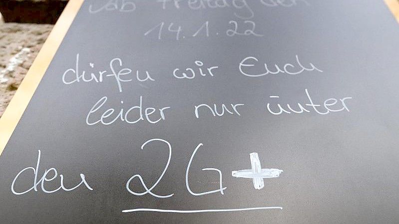 Auf einem Schild wird vor einem Cafe auf die 2G-plus-Regel hingewiesen. Wer genesen ist, behält diesen Status künftig nur noch drei statt sechs Monate. Foto: Robert Michael/dpa-Zentralbild/dpa