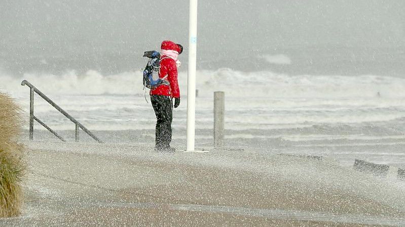 Eine Spaziergängerin auf Norderney blickt auf die Wellen der vom Sturm aufgepeitschten Nordsee. Foto: Volker Bartels/dpa