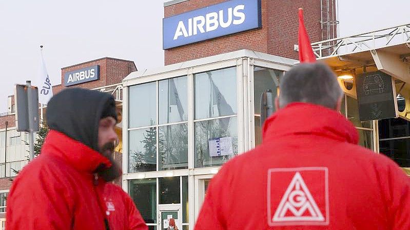 Mitglieder der IG Metall stehen vor einem Werkstor von Airbus in Hamburg-Finkenwerder. Foto: Bodo Marks/dpa