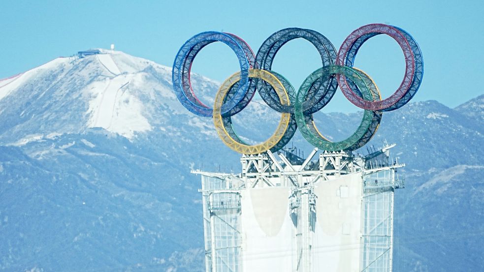 Der Blick auf die olympischen Ringe auf einem Turm in der Yanqing-Region. Im Hintergrund ist der Start der alpinen Olympia-Abfahrt am Xiaohaituo Mountain im Nationalen Ski-Alpin-Zentrum zu sehen. Die Olympischen Winterspiele in Peking finden vom 4. bis zum 20. Februar unter strengen Corona-Auflagen statt. Foto: DPA