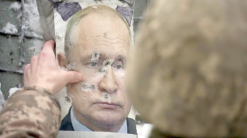 Ein ukrainischer Soldat justiert ein von Kugeln durchlöchertes Bild des russischen Präsidenten Putin. Foto: Vadim Ghirda/AP/dpa