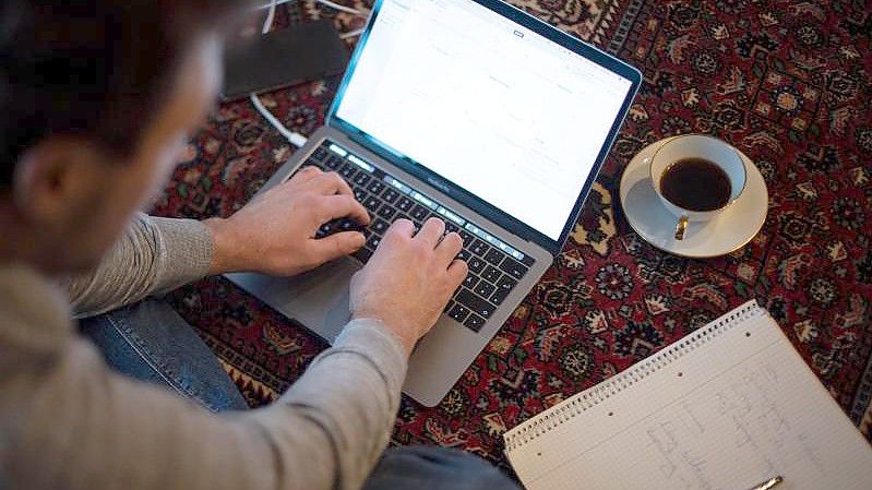 Ein Mann sitzt im Homeoffice mit Laptop auf dem Teppich und arbeitet. (Archivbild). Foto: Sina Schuldt/dpa