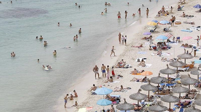 Touristen genießen an einem Strand bei Puerto Portals auf Mallorca die Sonne und das Meer. Der Klimawandel stellt die Reisebranche vor neue Herausforderungen. Foto: Clara Margais/dpa