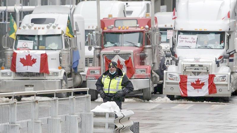 Ein Polizeibeamter steht vor Lastwagen, die die Straßen der Innenstadt von Ottawa blockieren. Foto: Patrick Doyle/The Canadian Press/AP/dpa