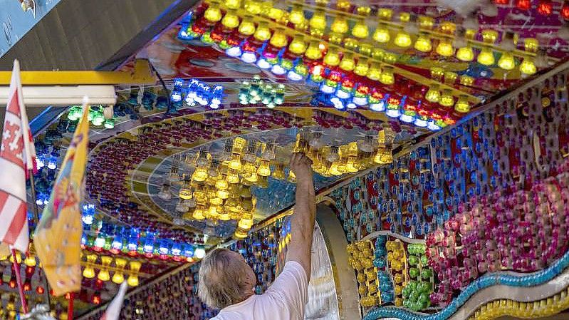Ein Mann schraubt Lampen in die Lichtinstallation eines Fahrgeschäfts. Der Verband hat auf die prekäre Lage der Schausteller in der Corona-Krise aufmerksam gemacht. Foto: David Inderlied/dpa