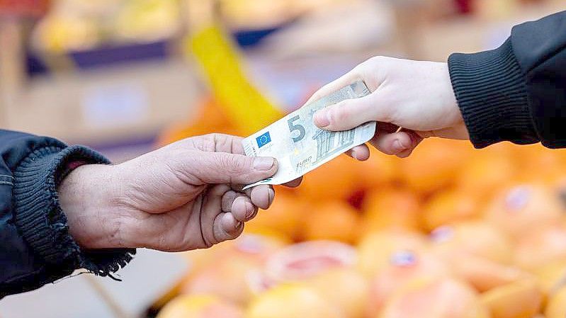 Ein Kunde bezahlt seinen Einkauf an einem Stand auf einem Wochenmarkt mit einem Fünf-Euro-Schein (gestellte Szene). Foto: Moritz Frankenberg/dpa