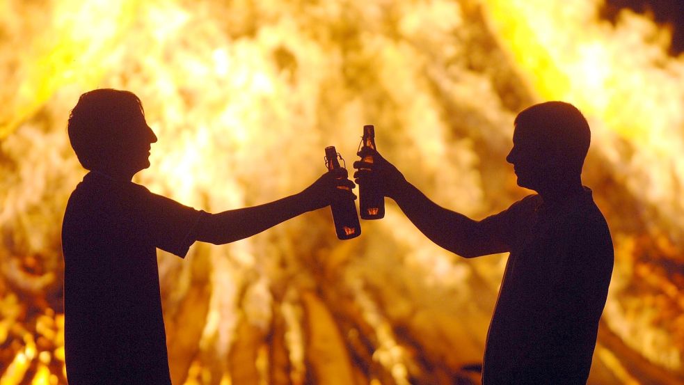 Zwei Jugendliche stoßen vor einem Feuer mit Bier an. Foto: DPA