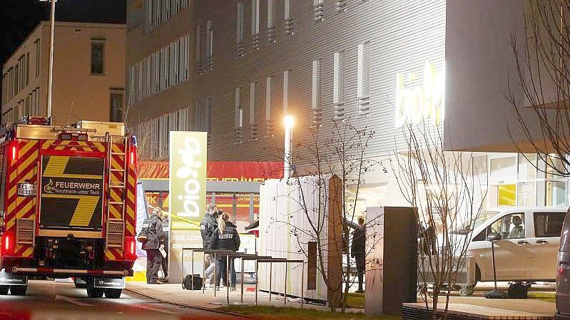 Polizisten und Feuerwehrleute stehen am Supermarkt in Kirchheim unter Teck, wo zwei Menschen durch Schüsse ums Leben gekommen sind. Foto: Andreas Rosar/Andreas Rosar Fotoagentur-Stuttg/dpa