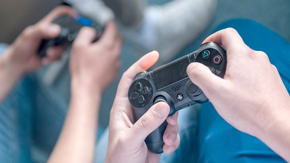 Ein Spieler hält einen Controller einer Spielkonsole in der Hand. Damit steuert er die Fußballer auf dem virtuellen Feld.Fotos: DPA