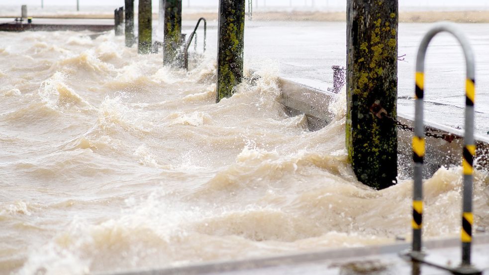 Wellen peitschen bei starkem Wind gegen eine Kaimauer im Fährhafen in Harlesiel. Durch den Sturm herrschen an der Küste erhöhte Wasserstände. Foto: DPA