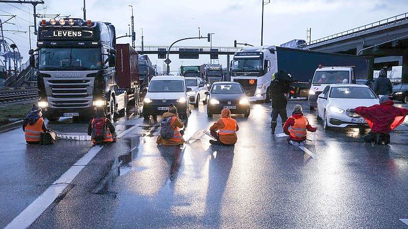 Klimaaktivisten der Aktion „Aufstand der letzten Generation“ blockierten am Montagmorgen in Hamburg eine Kreuzung am Zollamt Waltershof zur Köhlbrandbrücke und zur Autobahn A7. Foto: Christian Charisius/dpa