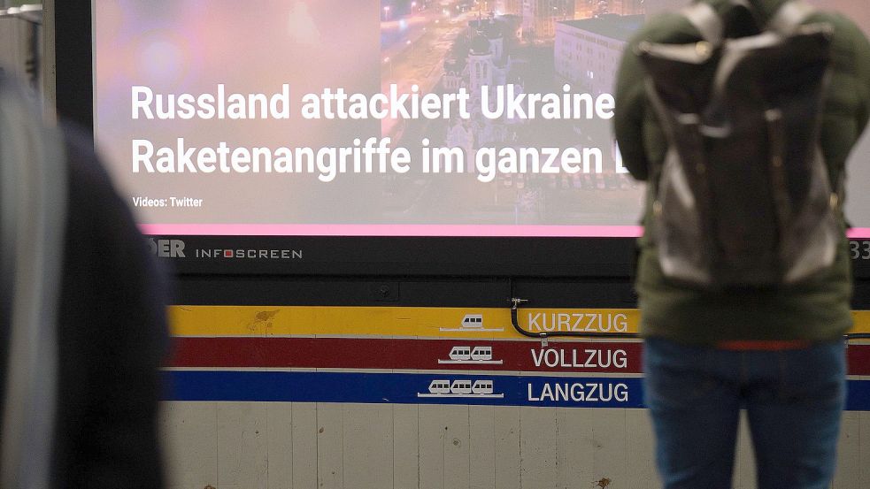 Menschen bleiben stehen und lesen: Nachrichten zum Ukraine-Konflikt werden auf einem Bildschirm im Frankfurter Hauptbahnhof angezeigt. Foto: DPA