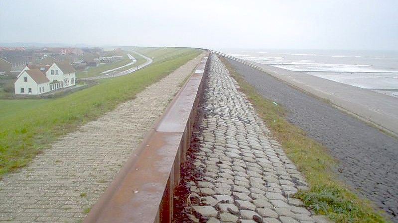 Ein Ort liegt an einem Deich hinter einem Strand in den Niederlanden. Foto: picture alliance / dpa