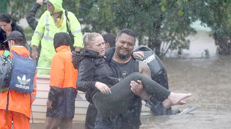 Ein Mann trägt eine Frau durch das Hochwasser einer überschwemmten Straße im australischen Lismore. Foto: Jason O‚äôbrien/AAP/dpa