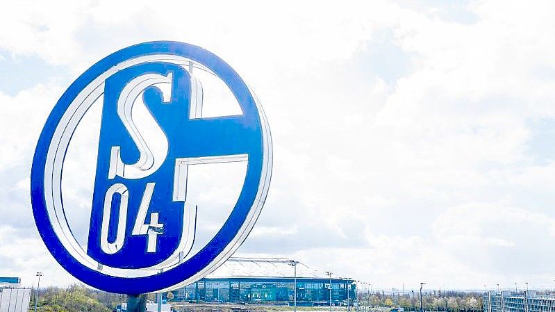 Im Vordergrund dreht sich das Logo des FC Schalke auf der Geschäftsstelle, im Hintergrund steht die Veltins-Arena. Foto: Guido Kirchner/dpa
