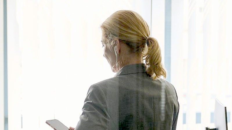 Eine Frau steht in einem Bürozimmer und hält ein Smartphone in der Hand (gestellte Szene). Foto: Annette Riedl/dpa