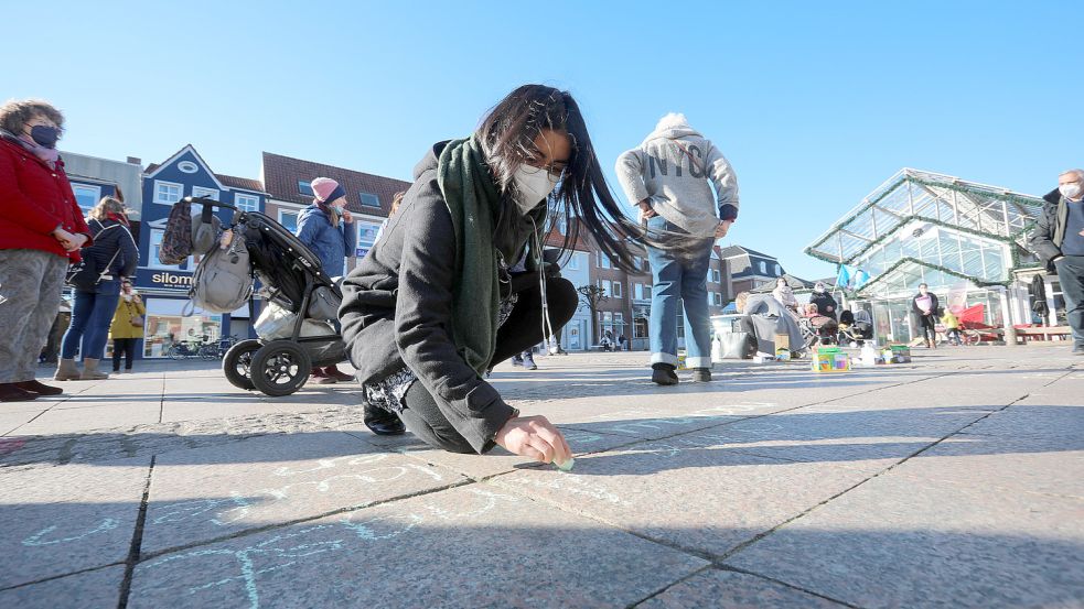 Eine Frau schreibt die Worte „Ich will ohne Angst nach Hause laufen können“ auf das Pflaster des Marktplatzes. Foto: Romuald Banik